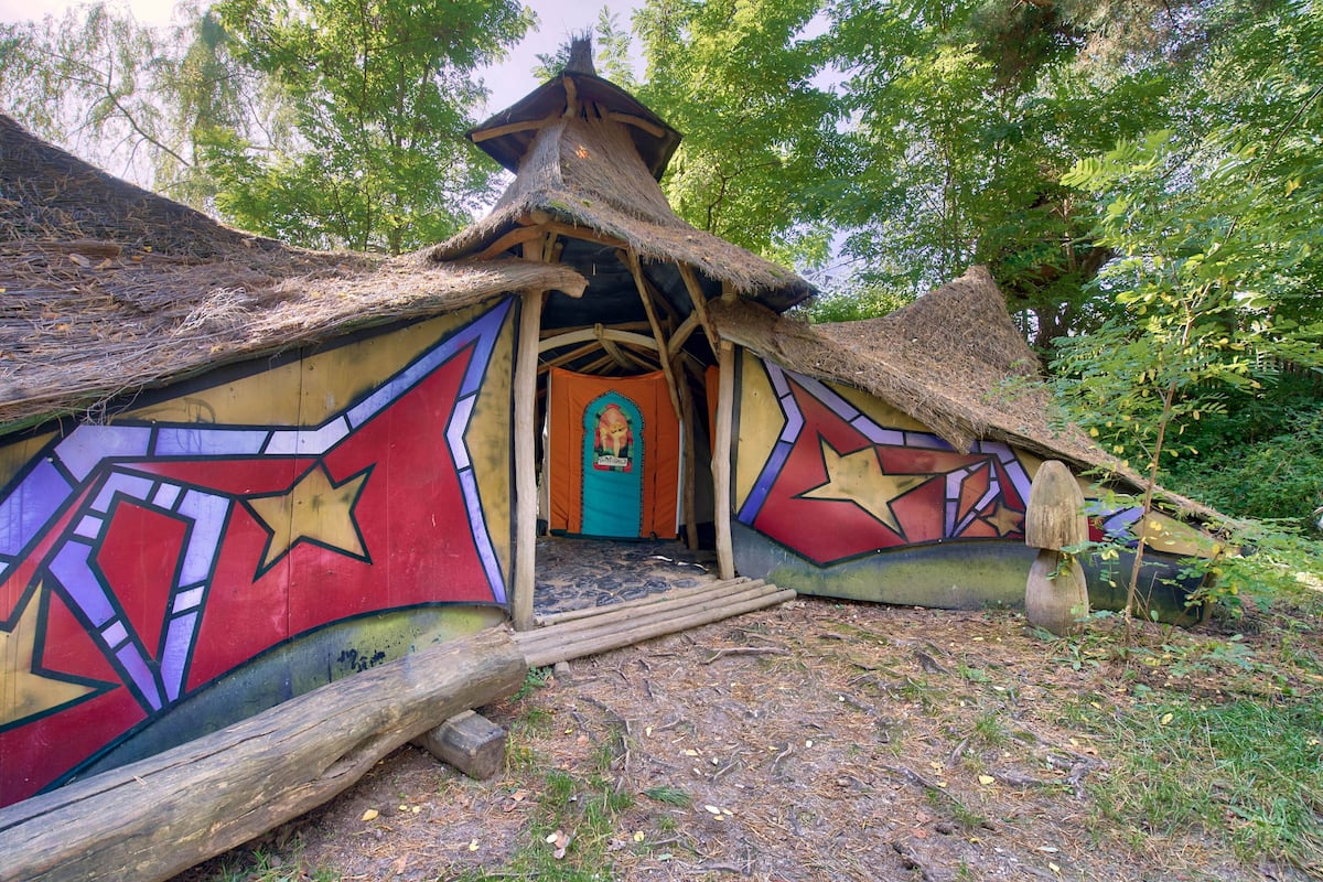 A traditional thatched-roof structure with colorful geometric patterns, a central doorway, and a small porch area.