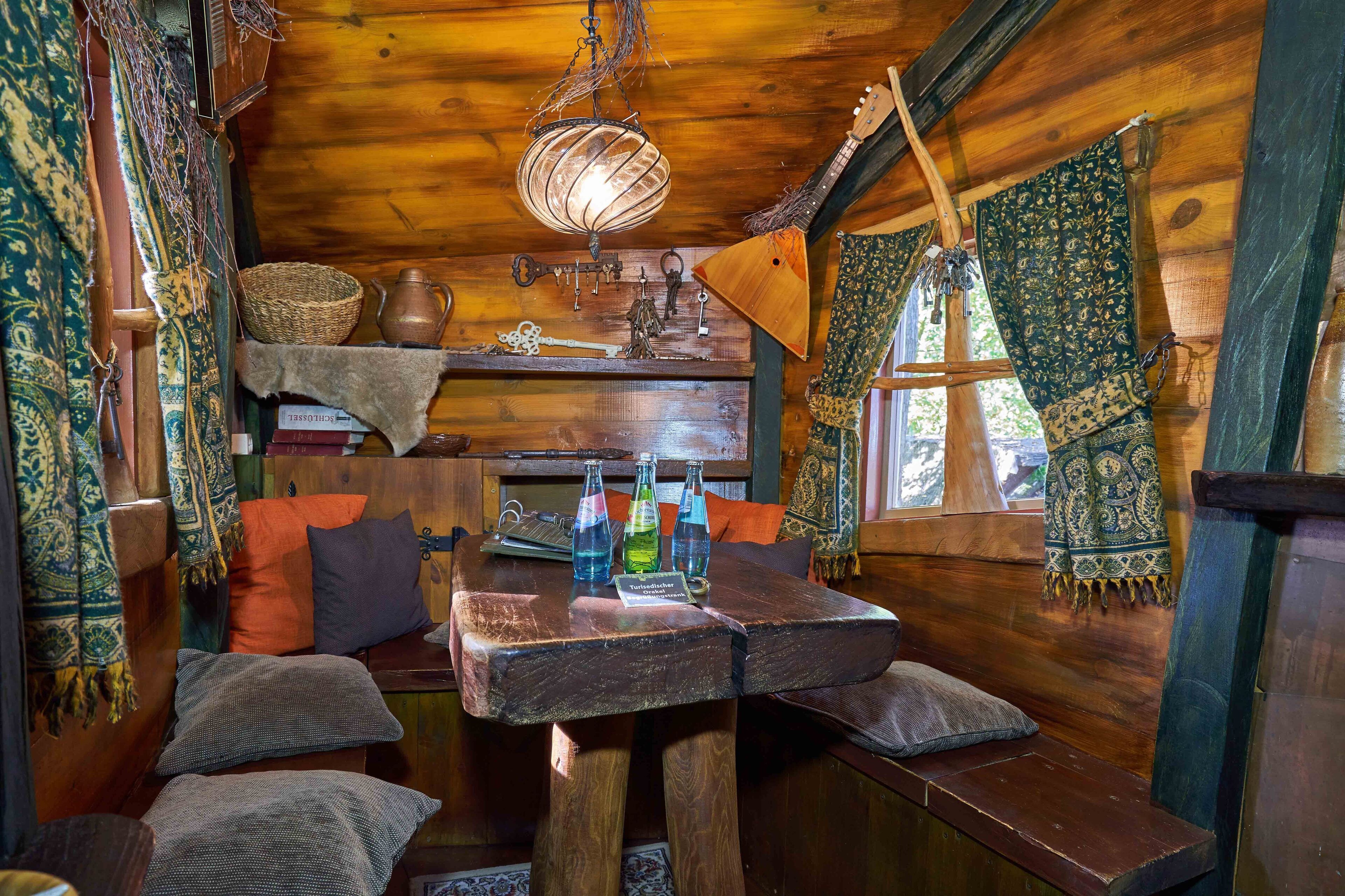 Ein gemütliches Blockhaus-Interieur mit Holztisch, Bänken, einer Hängelampe und verschiedenen Dekorationselementen.