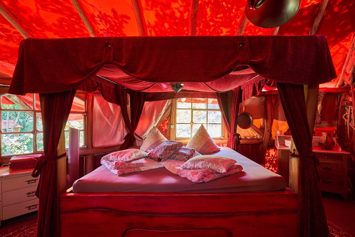 A bed with a canopy, multiple pillows, and a window with curtains.