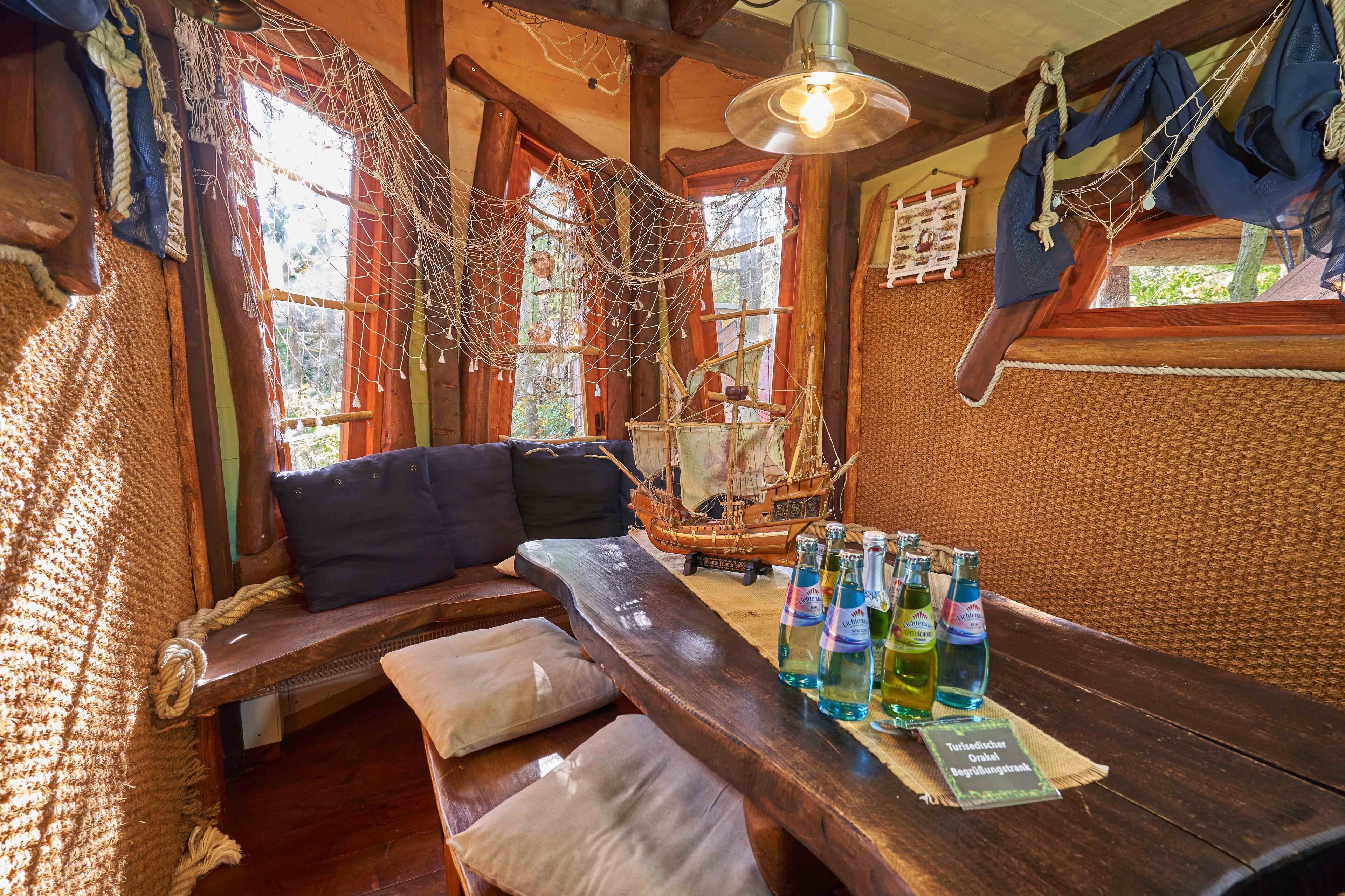 Un banco de madera con almohadones, una mesa con botellas y un modelo de barco.