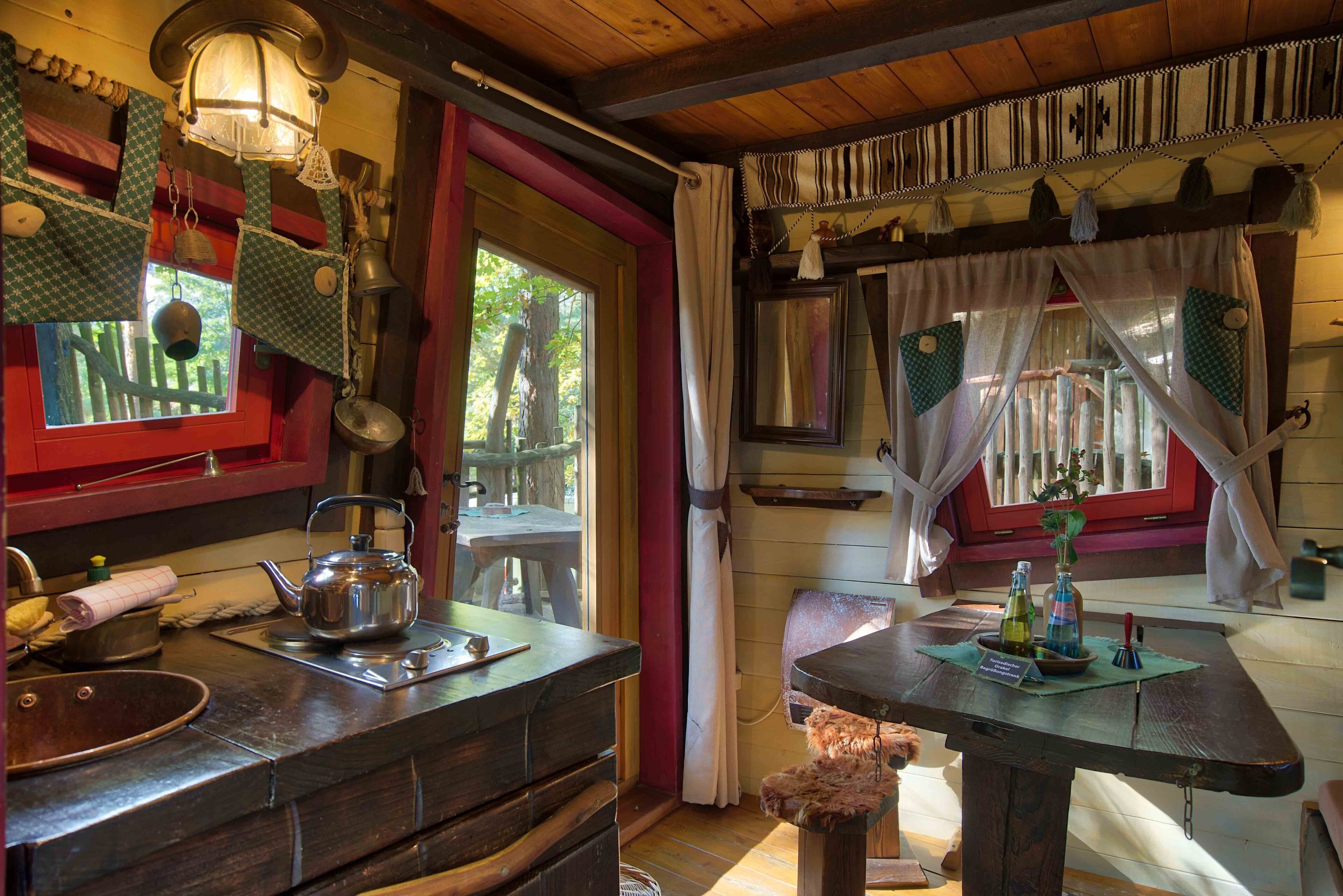 Una cocina rústica con una mesa de madera, un hervidor y una ventana con cortinas.