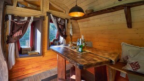 A wooden cabin interior with a wooden table, a hanging light fixture, and a window with curtains. - Die Geheime Welt von Turisede (Neisseaue)
