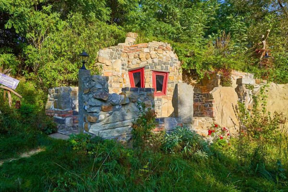 A rustic stone structure with a red door, surrounded by lush greenery.
