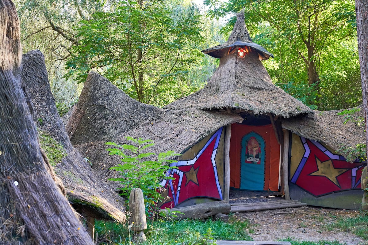 A thatched-roof hut with colorful murals, surrounded by trees.