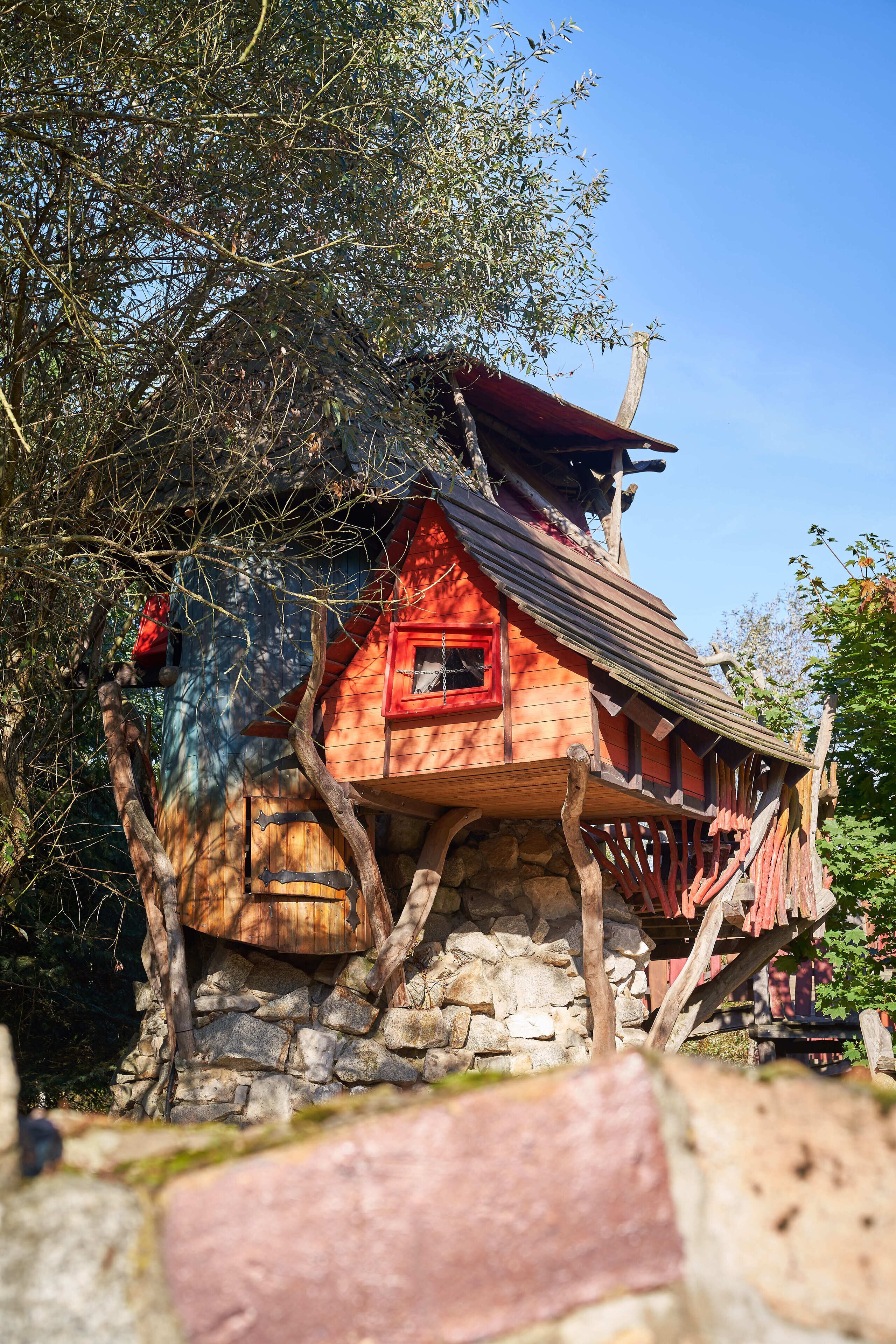 A treehouse with a stone base, wooden beams, and a red roof.