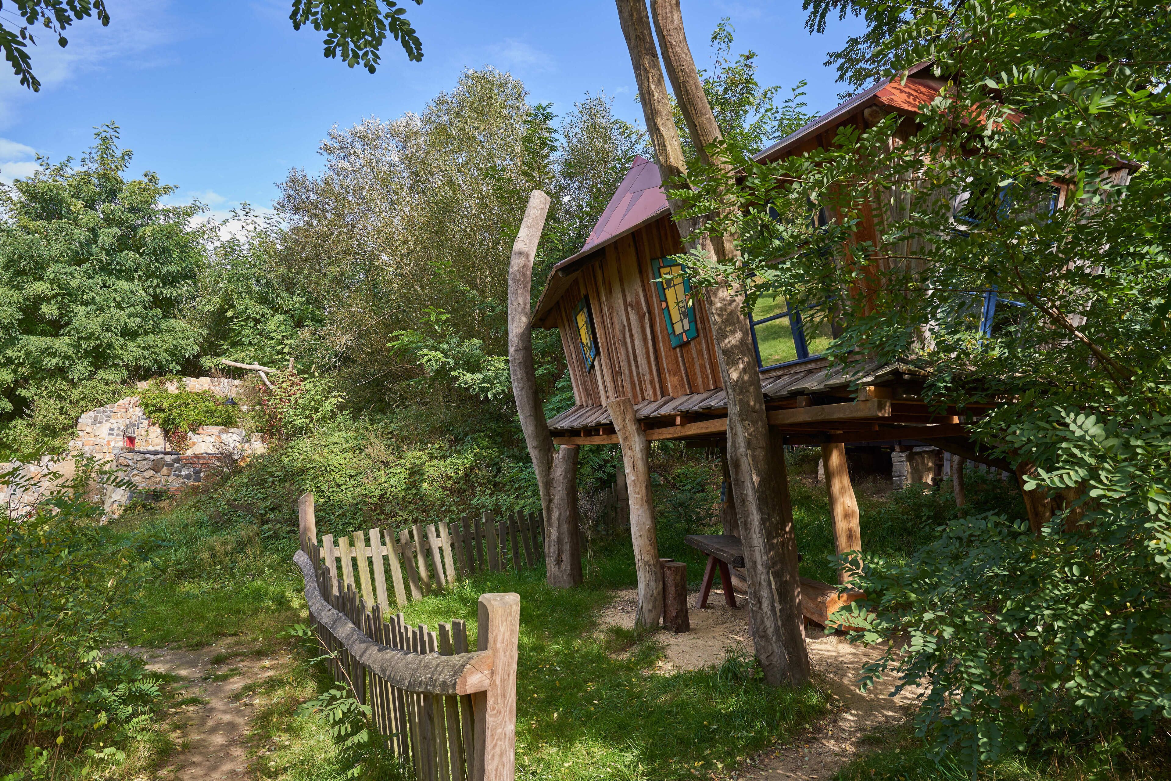 Una casa di legno rustica con tetto rosso, immersa nel verde e circondata da un recinto in legno.