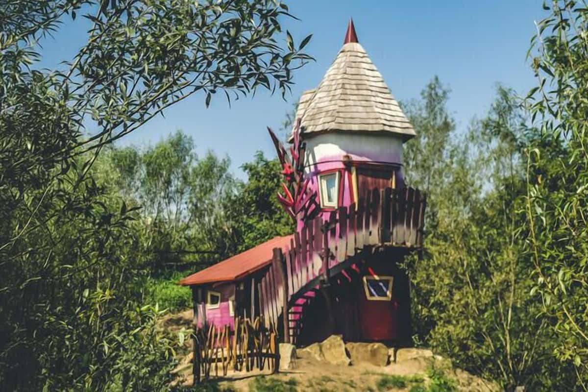 A unique, colorful treehouse with a conical roof, surrounded by dense foliage.