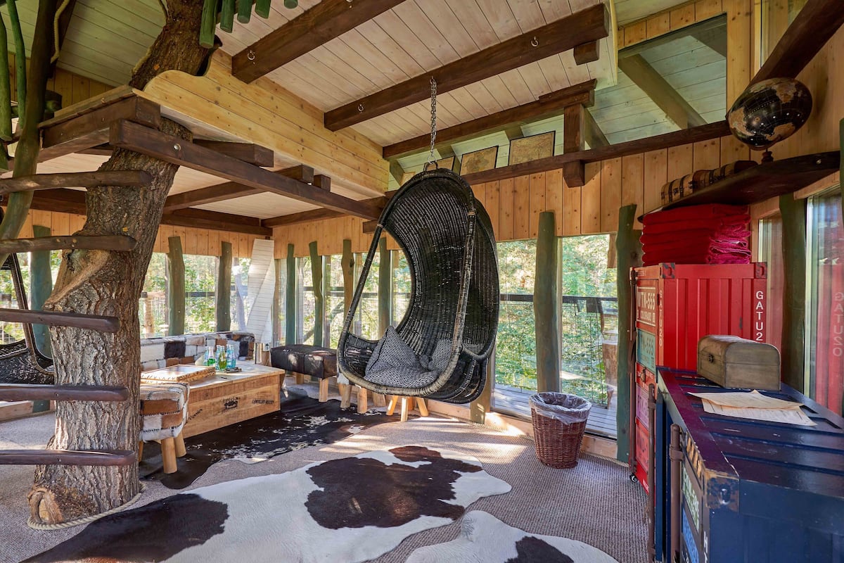A rustic wooden interior with a hanging chair, wooden table, and a cowhide rug.