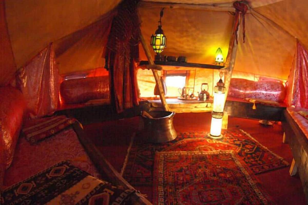 A cozy tent interior with a central seating area, a table with a kettle, and a hanging light fixture.