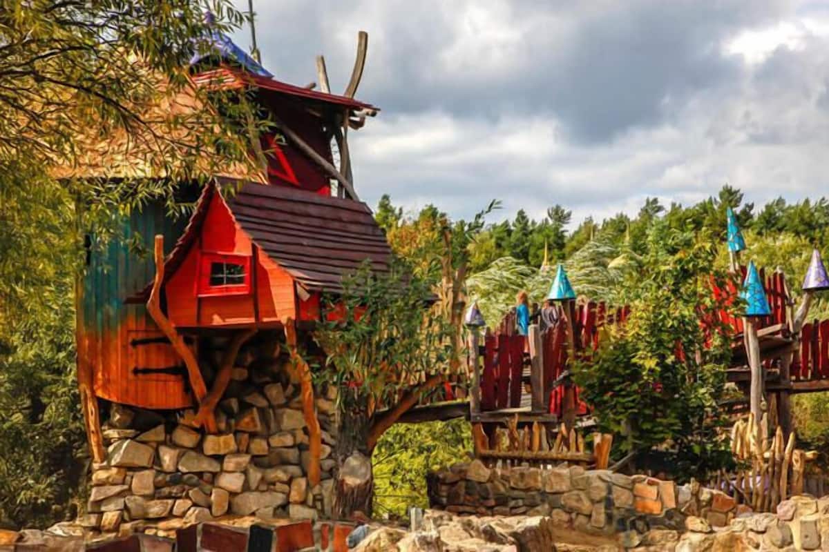 A rustic wooden structure with a stone base, surrounded by lush greenery and a wooden fence.