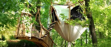 A treehouse with a wooden bridge and a hanging platform.