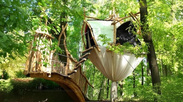 Una casa en el árbol con un puente de madera y una plataforma colgante.