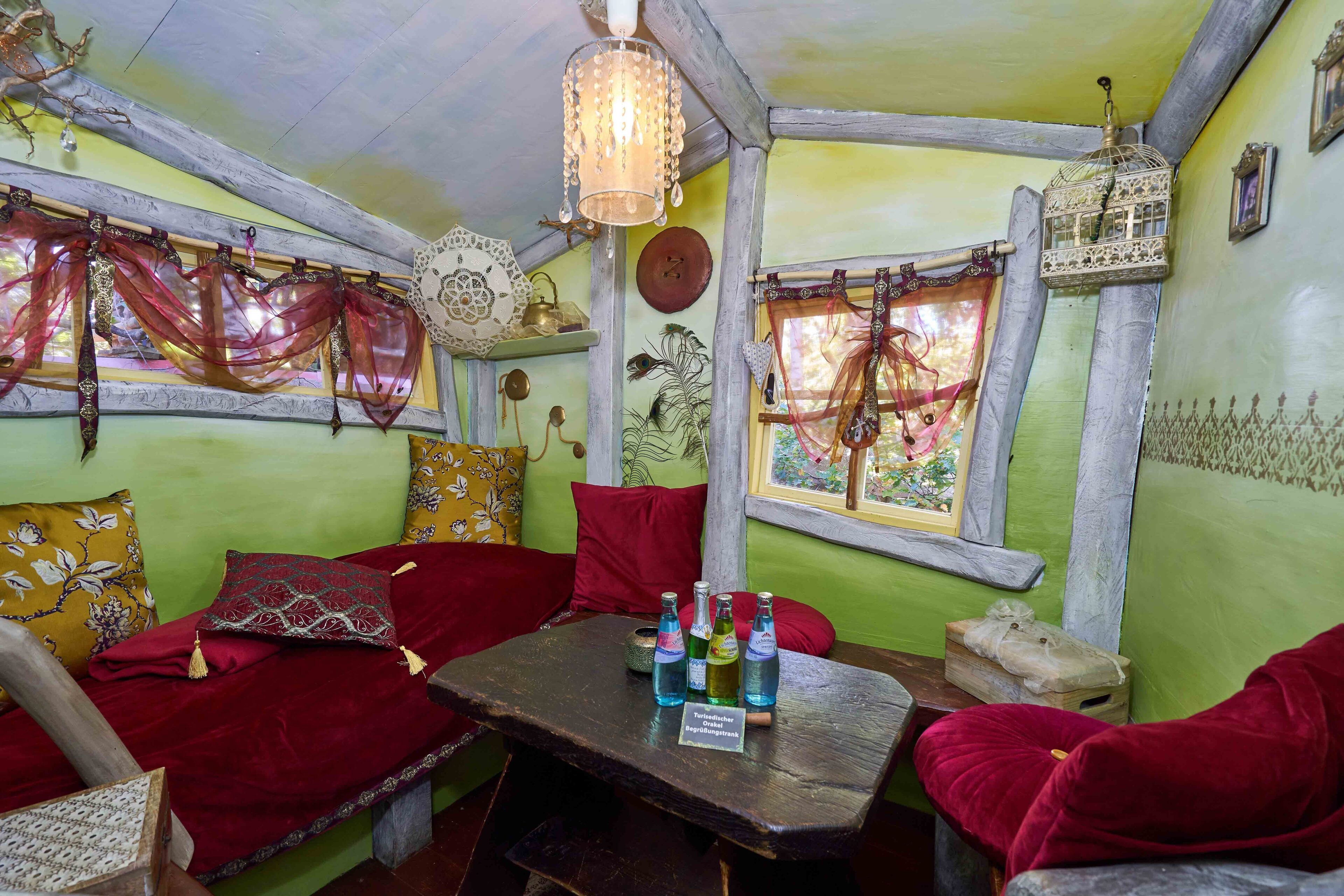 A cozy room with a wooden table, red cushions, and a hanging birdcage.