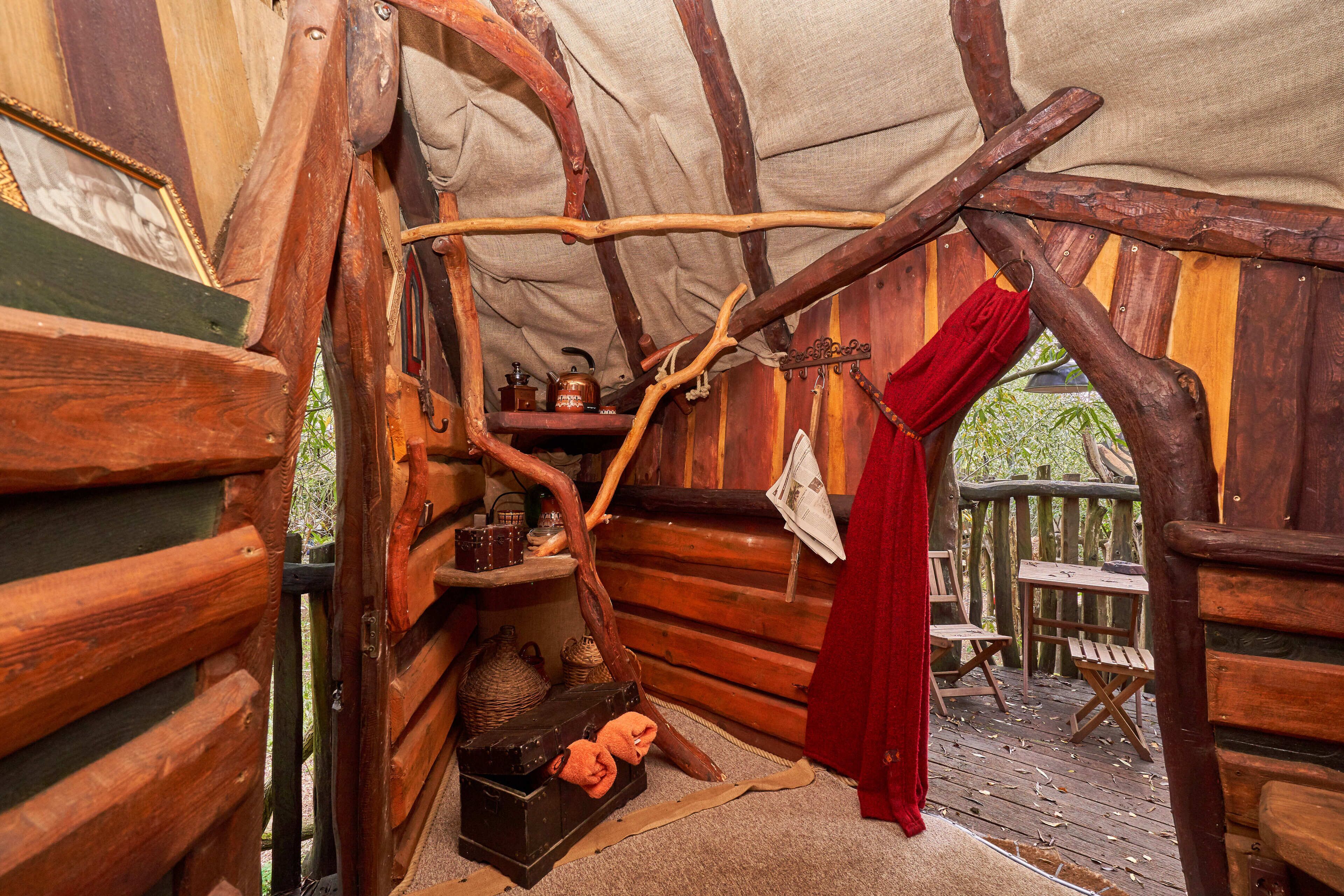 A rustic wooden cabin interior with a wooden bench, a small table, and a hanging red curtain.
