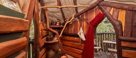 A rustic wooden cabin interior with a wooden bench, a small table, and a hanging red curtain.