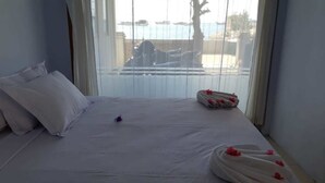 A hotel room with a bed, pillows, a neatly made bedspread, and a view of the sea through the window. - Bajo Sunset Hostel (Labuan Bajo)