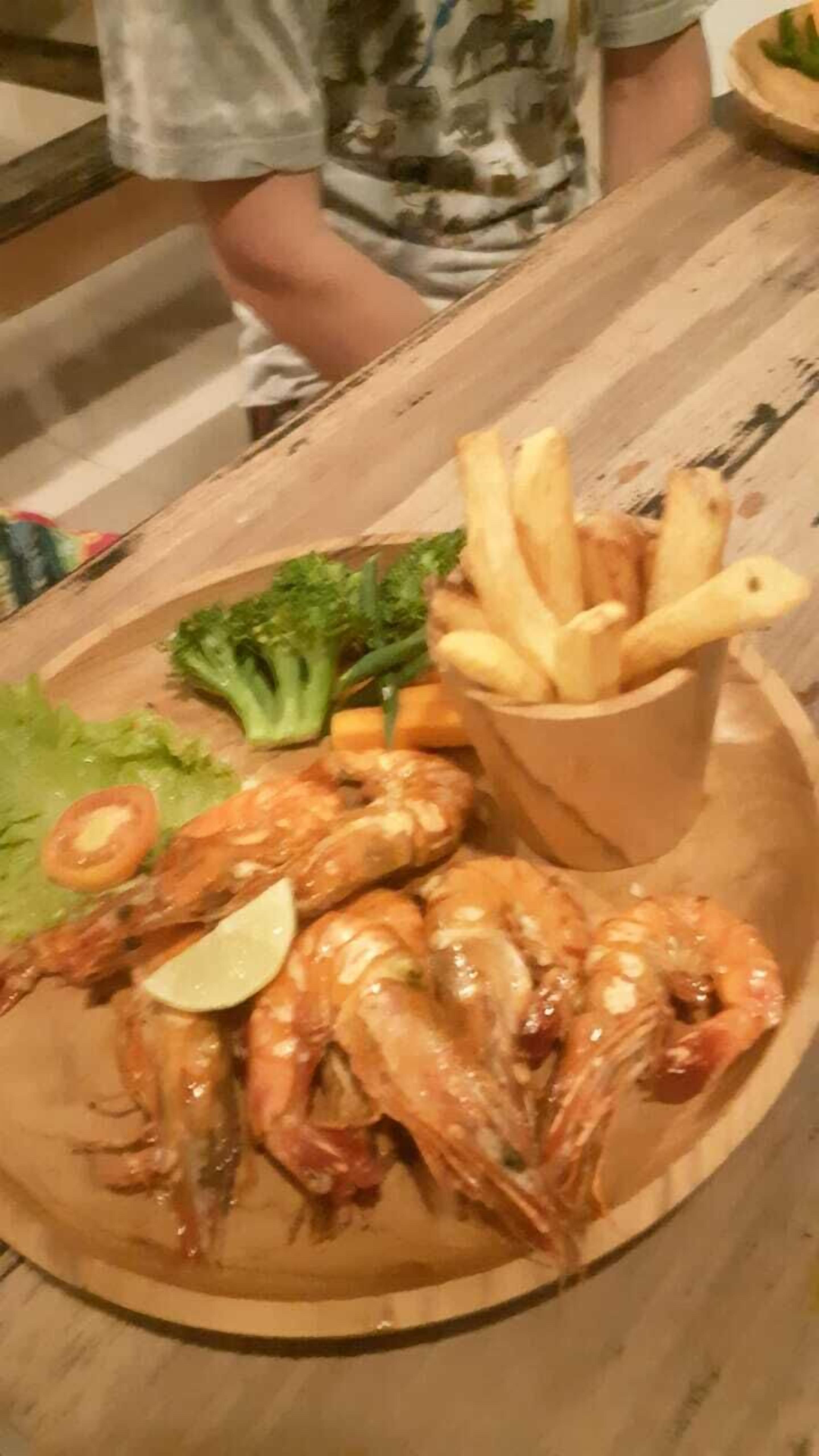 Une table en bois sur laquelle est disposée une assiette de fruits de mer comprenant des crevettes, des tranches de citron, de la laitue et une portion de frites.
