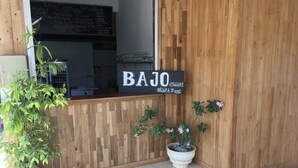 A wooden reception desk with a sign reading "BAJO Sunsets, Hostel & Resto." - Bajo Sunset Hostel (Labuan Bajo)