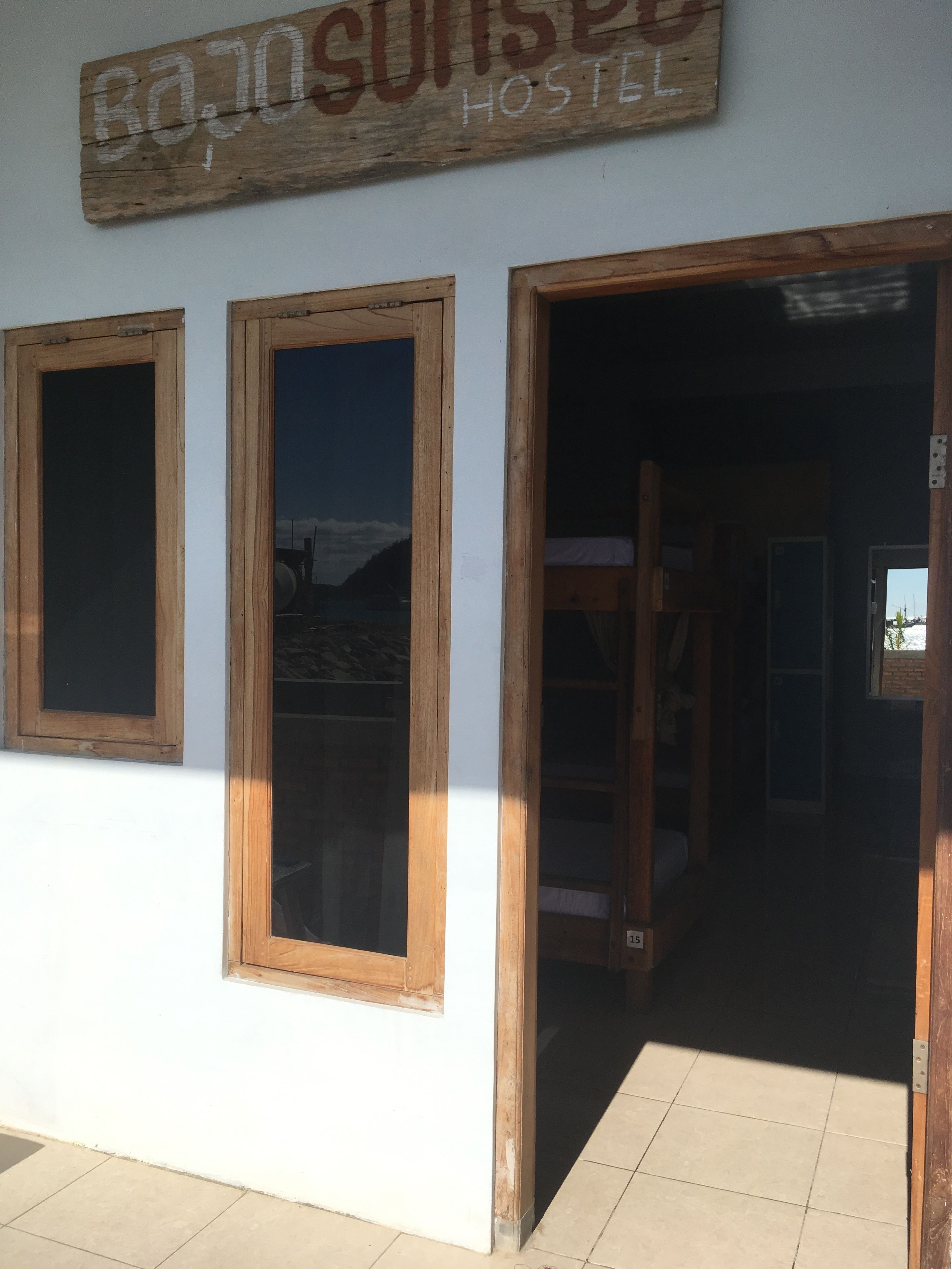 A hostel entrance with wooden-framed windows and a sign reading "Baño Sunrise Hostel".