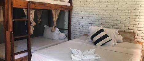 Un lit superposé avec une literie blanche et un oreiller à rayures, une échelle en bois et un mur en briques blanches.