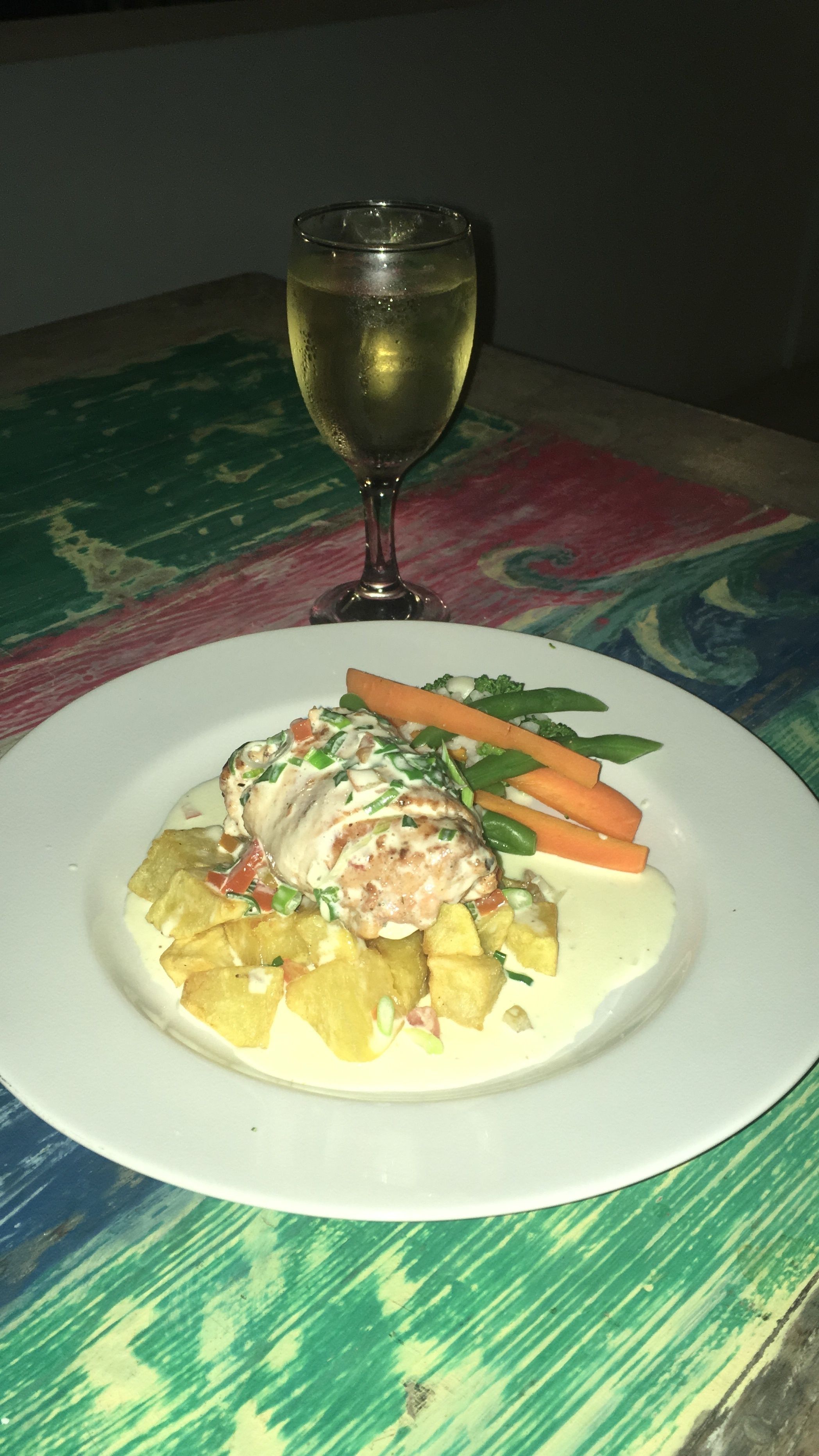 A plate of food with a glass of white wine on a table with a colorful tablecloth.