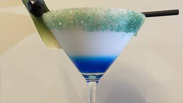 A martini glass with a blue and white layered drink, a sugar rim, and a green leaf garnish on a wooden table.