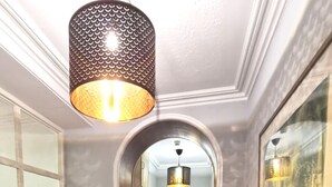 A hallway with a dark gray sofa, a patterned pendant light, and a framed artwork on the wall. - Lunan House (Arbroath)