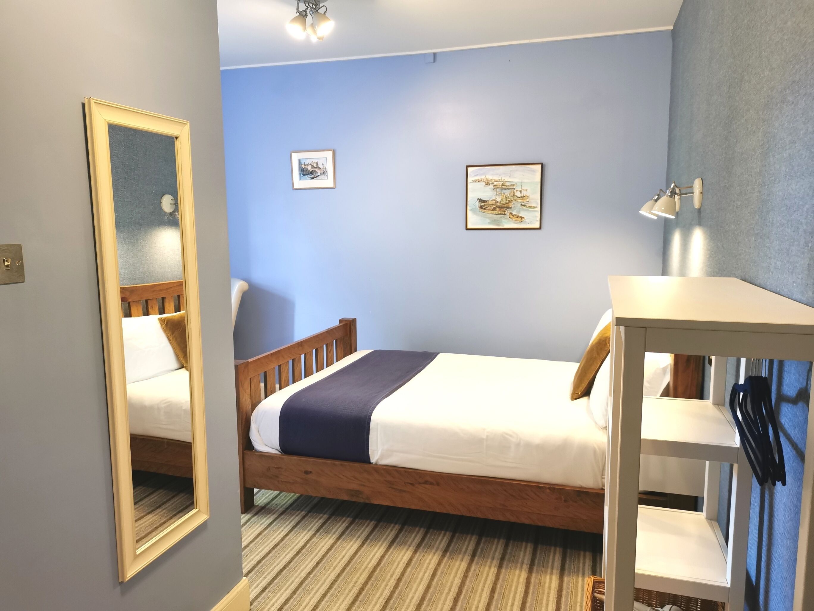 Un dormitorio con una cama de madera, un espejo, dos cuadros en la pared y una mesita de noche con una lámpara.