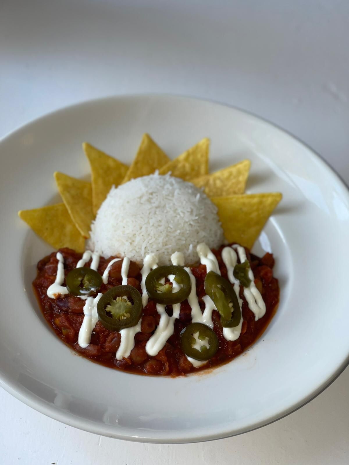 A plate with white rice, refried beans, jalapeños, and a white sauce, accompanied by tortilla chips.