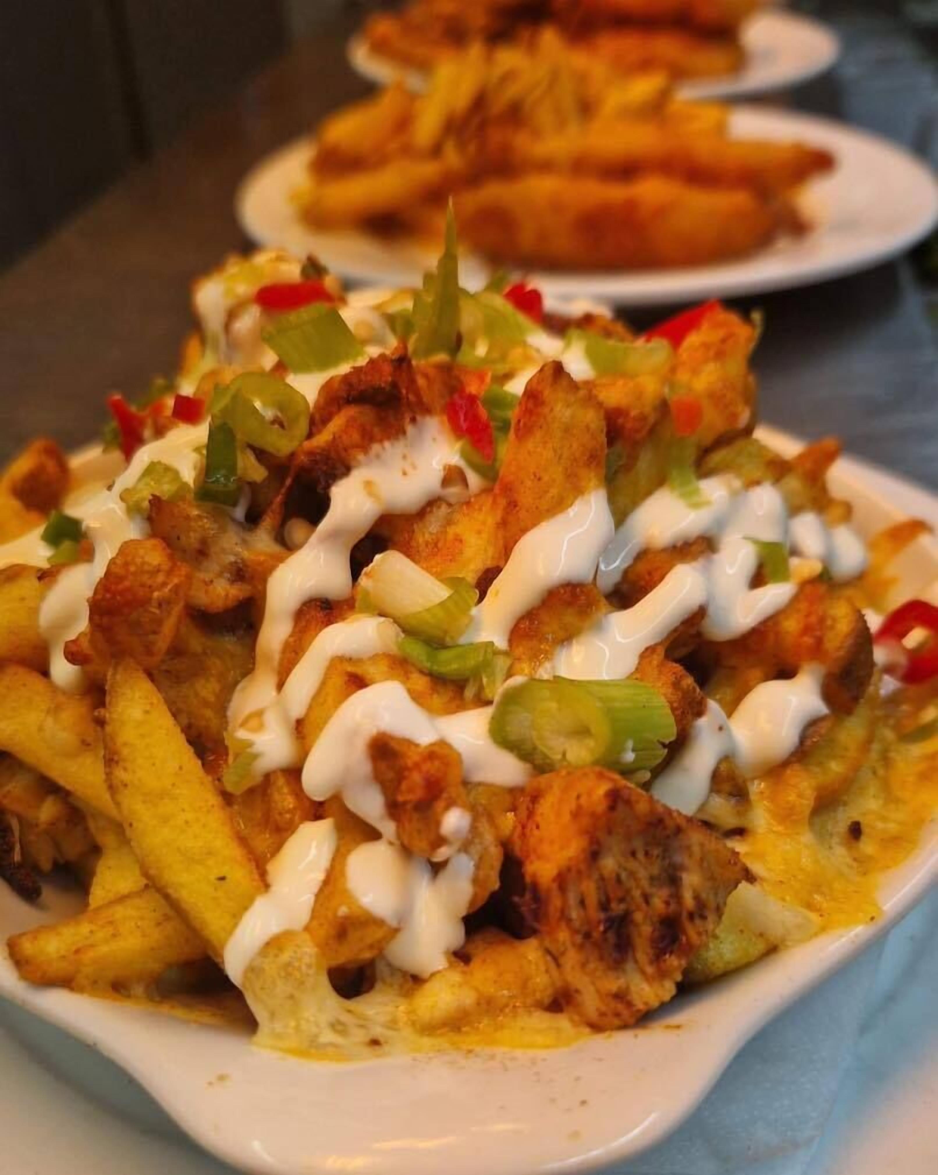 A plate of nachos topped with chicken, cheese, and green peppers, served with a white sauce.