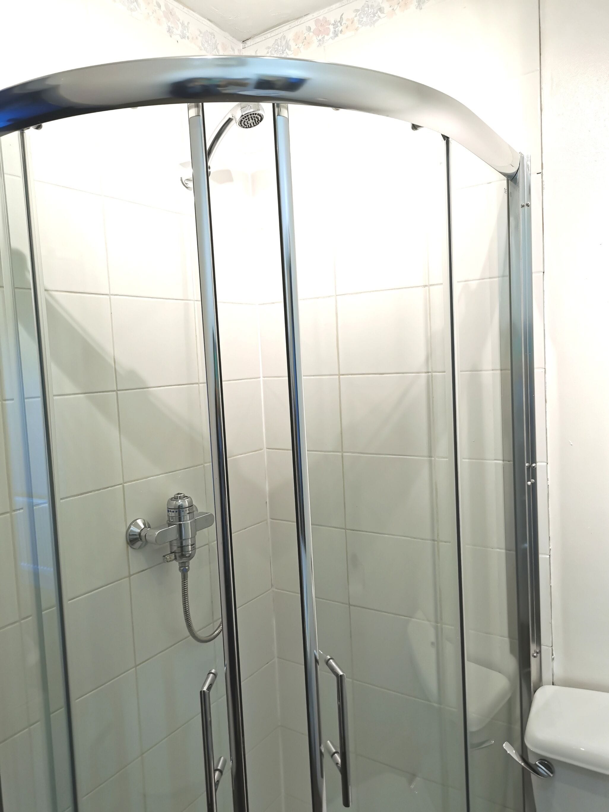 A glass-enclosed shower stall with a handheld showerhead and a handheld shower attachment.