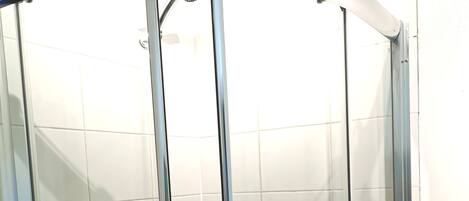 A glass-enclosed shower stall with a handheld showerhead and a handheld shower attachment.