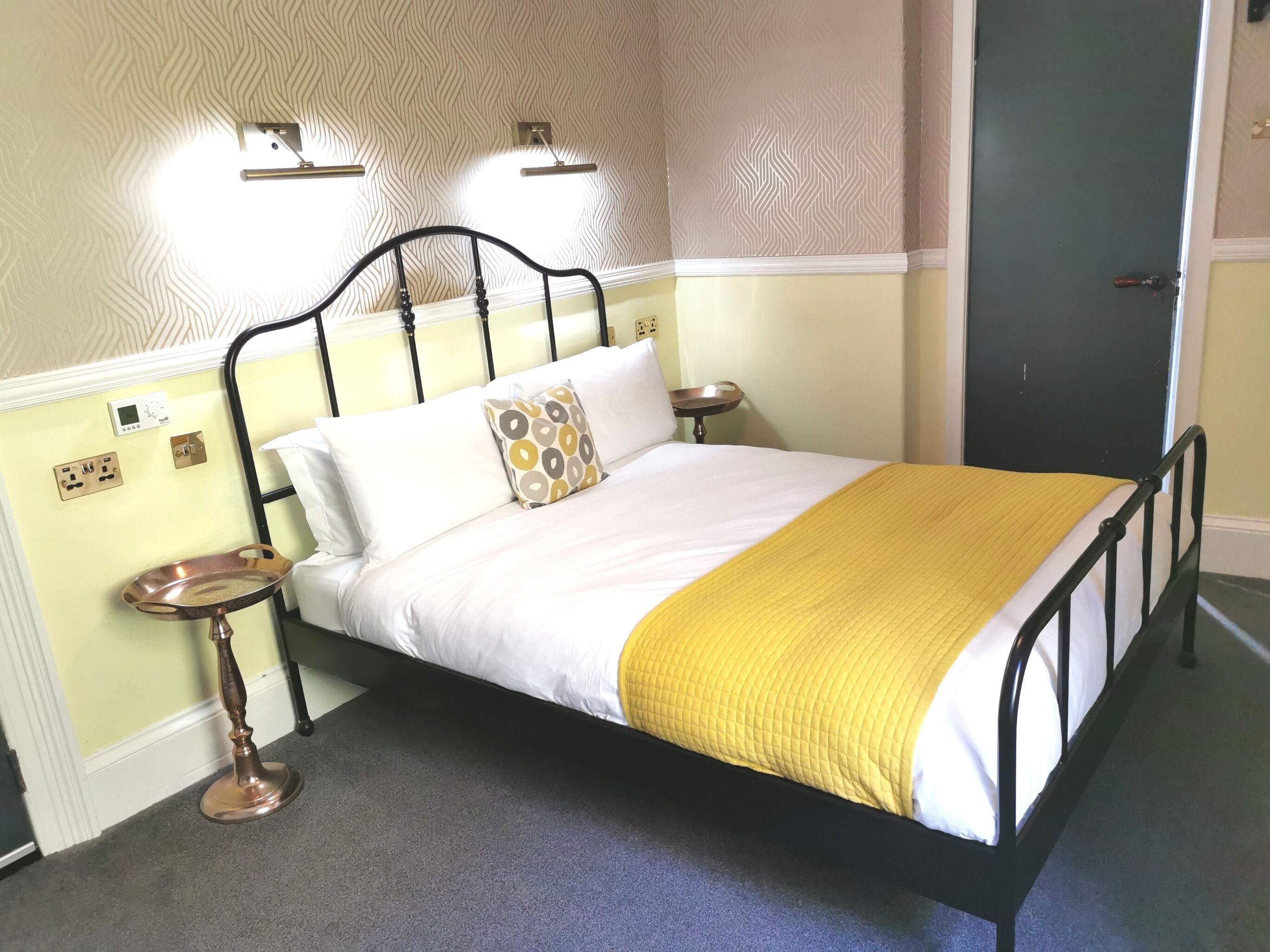 A neatly made bed with a yellow blanket, a bedside table with a lamp, and a wall-mounted light fixture.