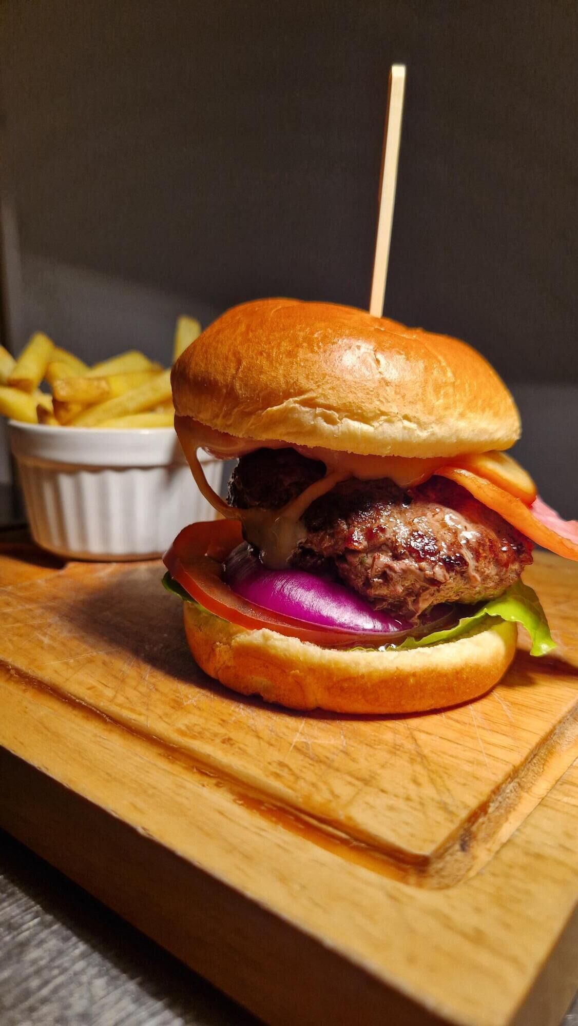 A burger with a bun, lettuce, tomato, and cheese, accompanied by a side of fries.