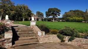 A stone staircase leading to a grassy area with a large tree and a building in the background. - Lunan House (Arbroath)