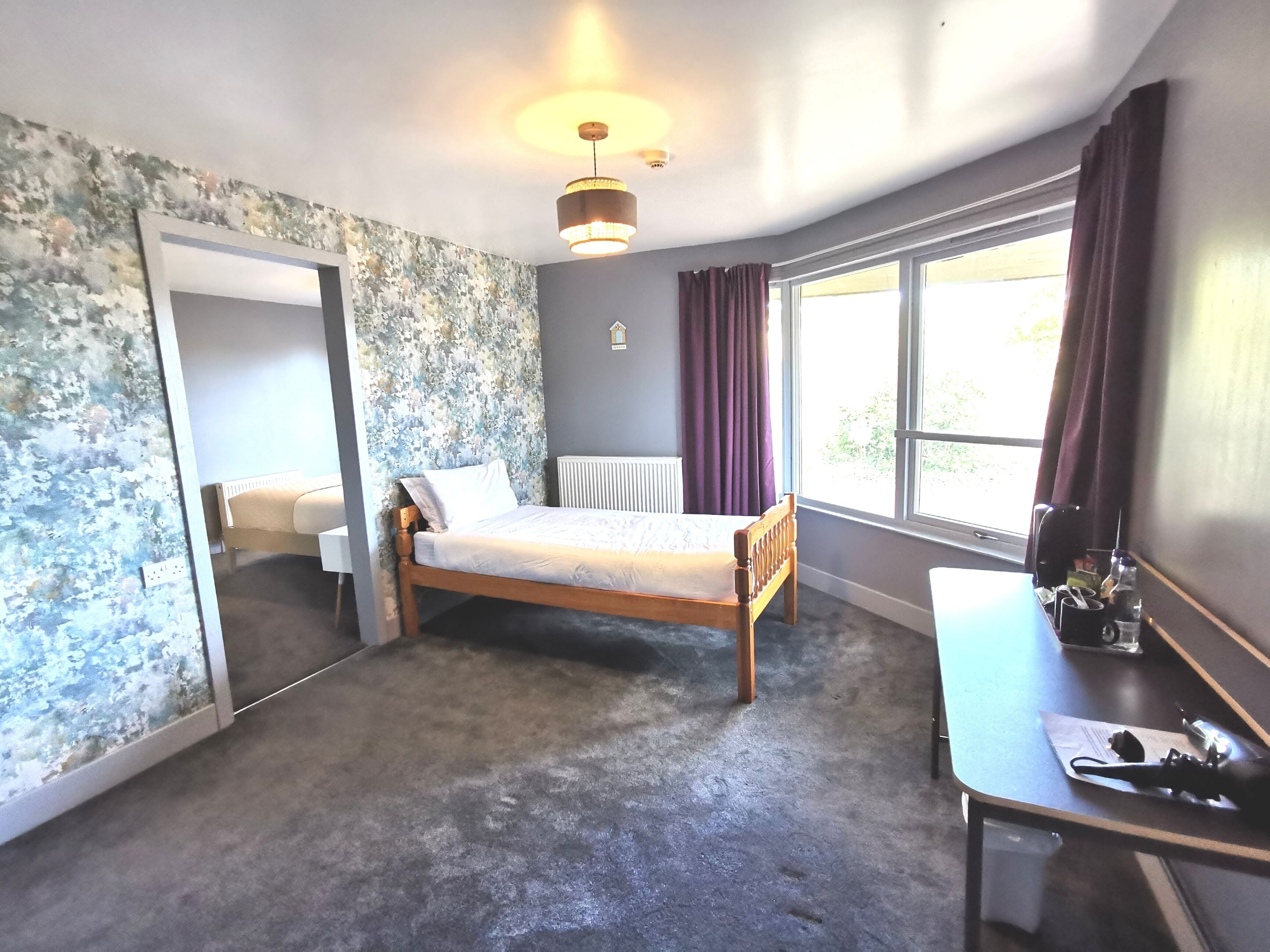 Een slaapkamer met een bed, een bureau, een radiator en een raam met gordijnen.