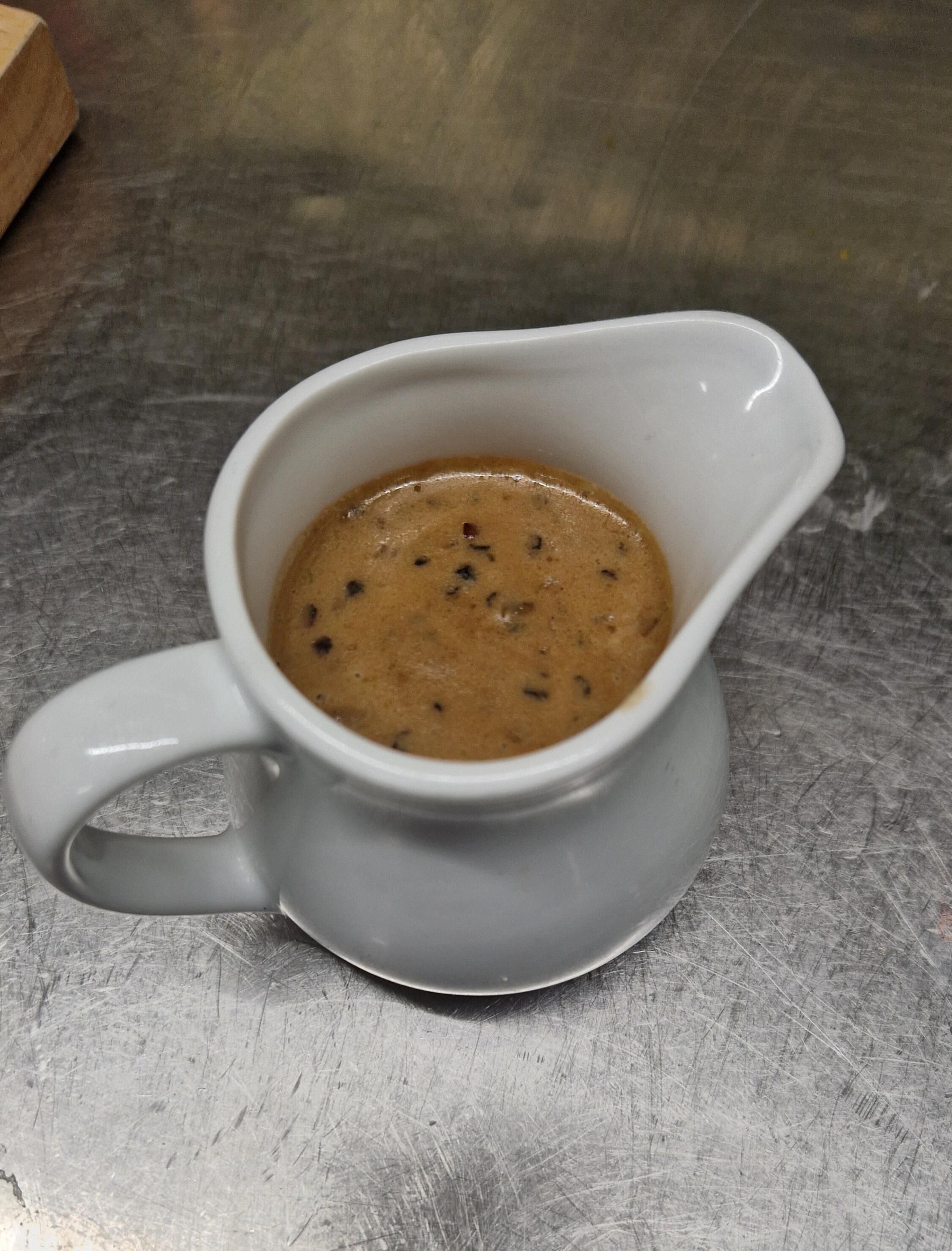 A white ceramic pitcher filled with a brown liquid, possibly coffee, on a metallic surface.