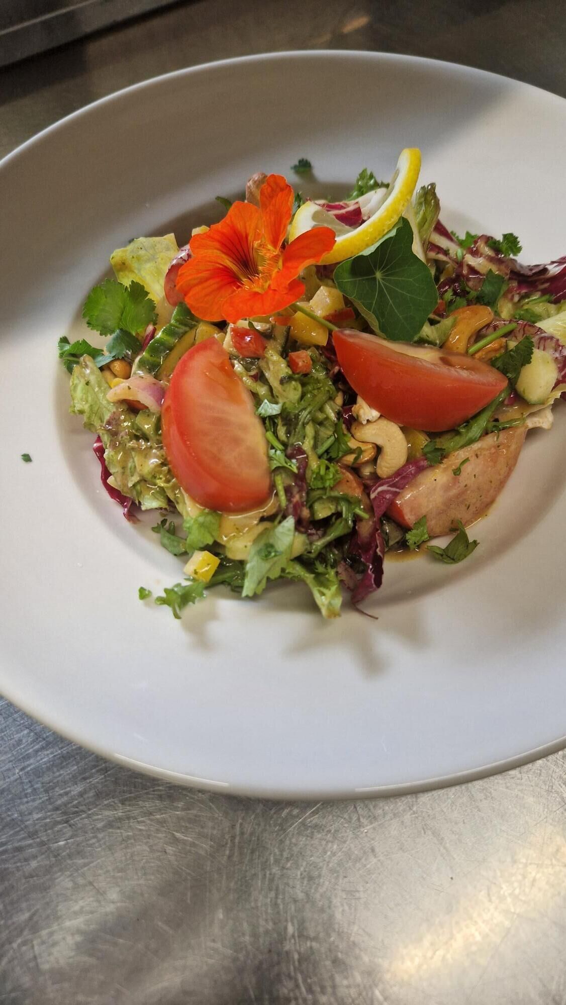 A plate of mixed greens salad with tomatoes, nuts, and a decorative flower.