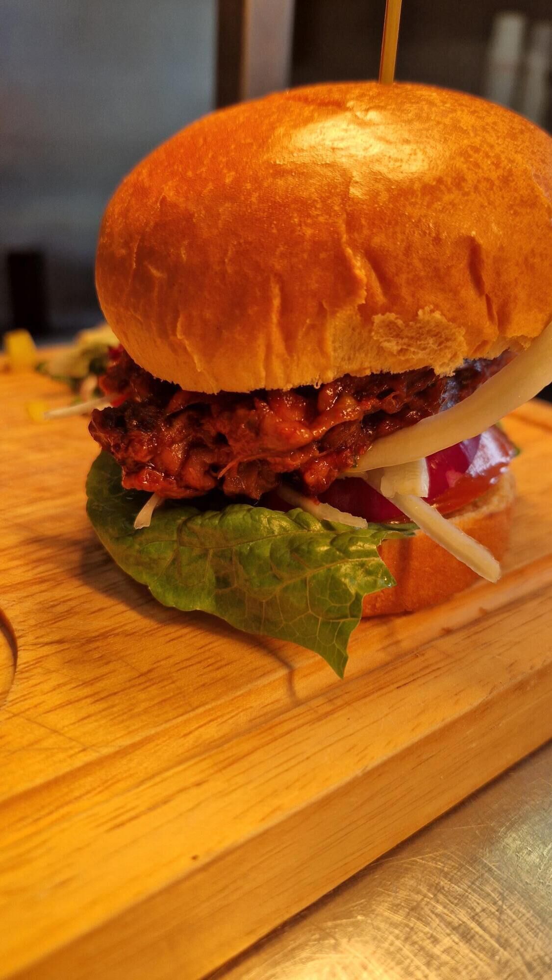 Un sandwich préparé avec un pain grillé, de la laitue et une garniture à base de viande, le tout posé sur une surface en bois.