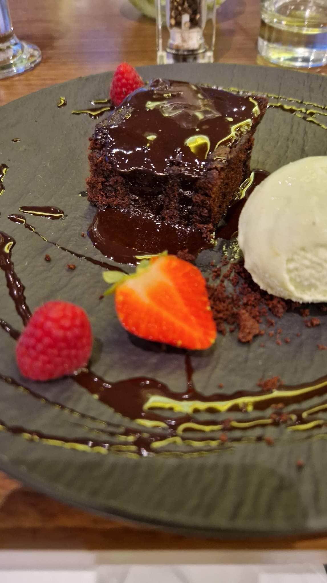 Un plato de postre con pastel de chocolate, fresas y una porción de helado.
