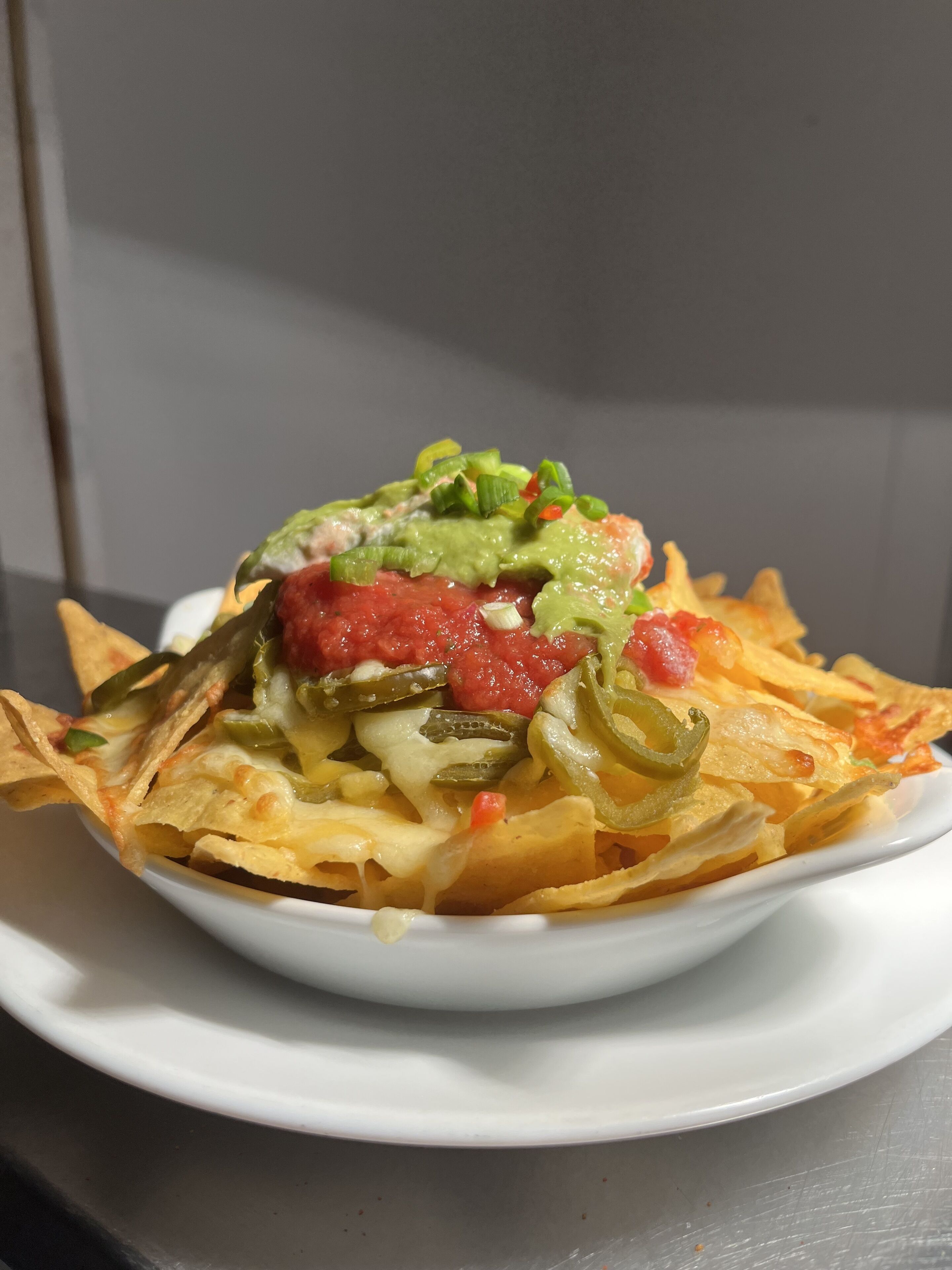A bowl of nachos topped with cheese, jalapeños, and a red sauce.