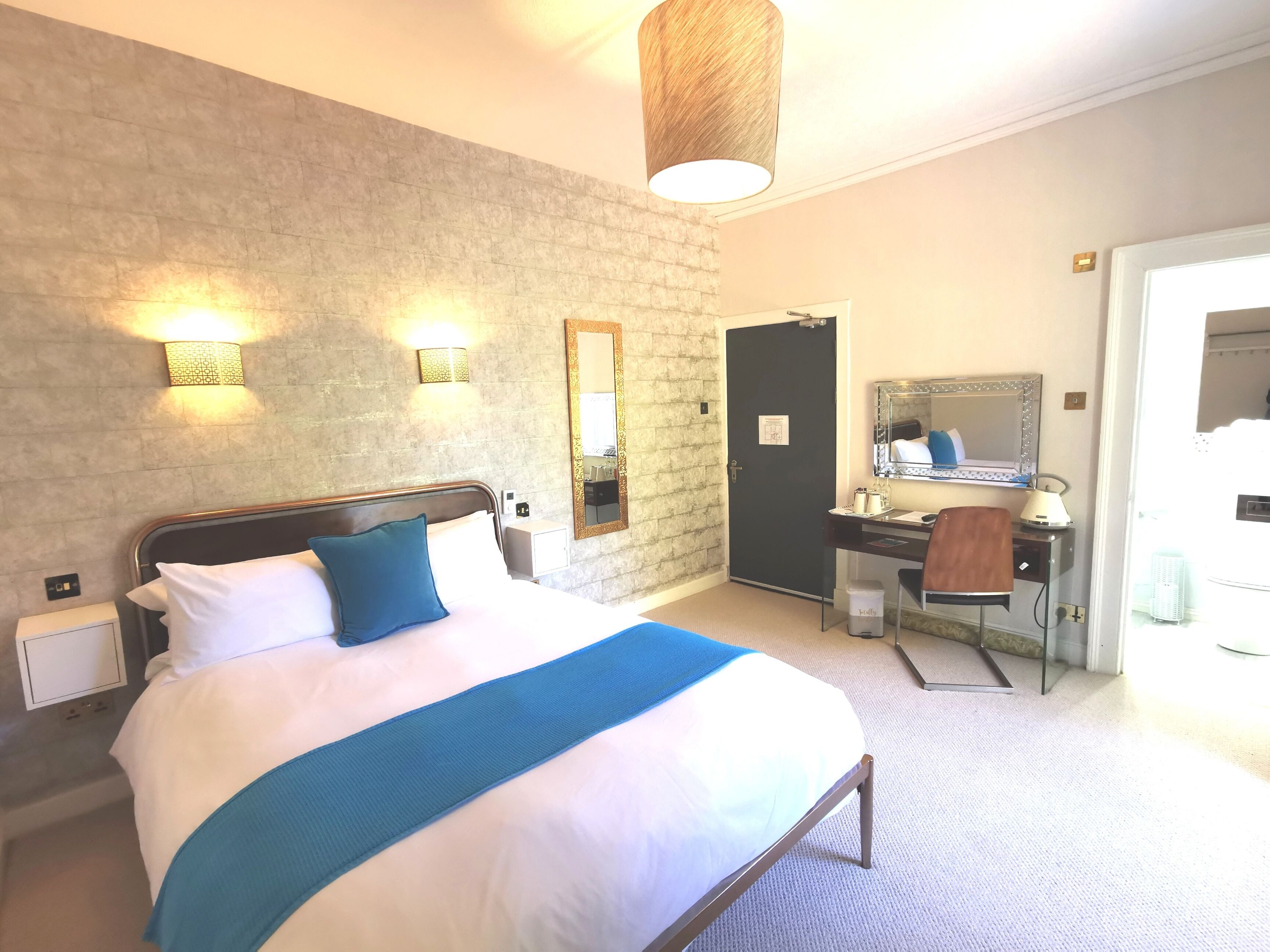 A hotel room with a bed, bedside table, desk, chair, and a mirror.