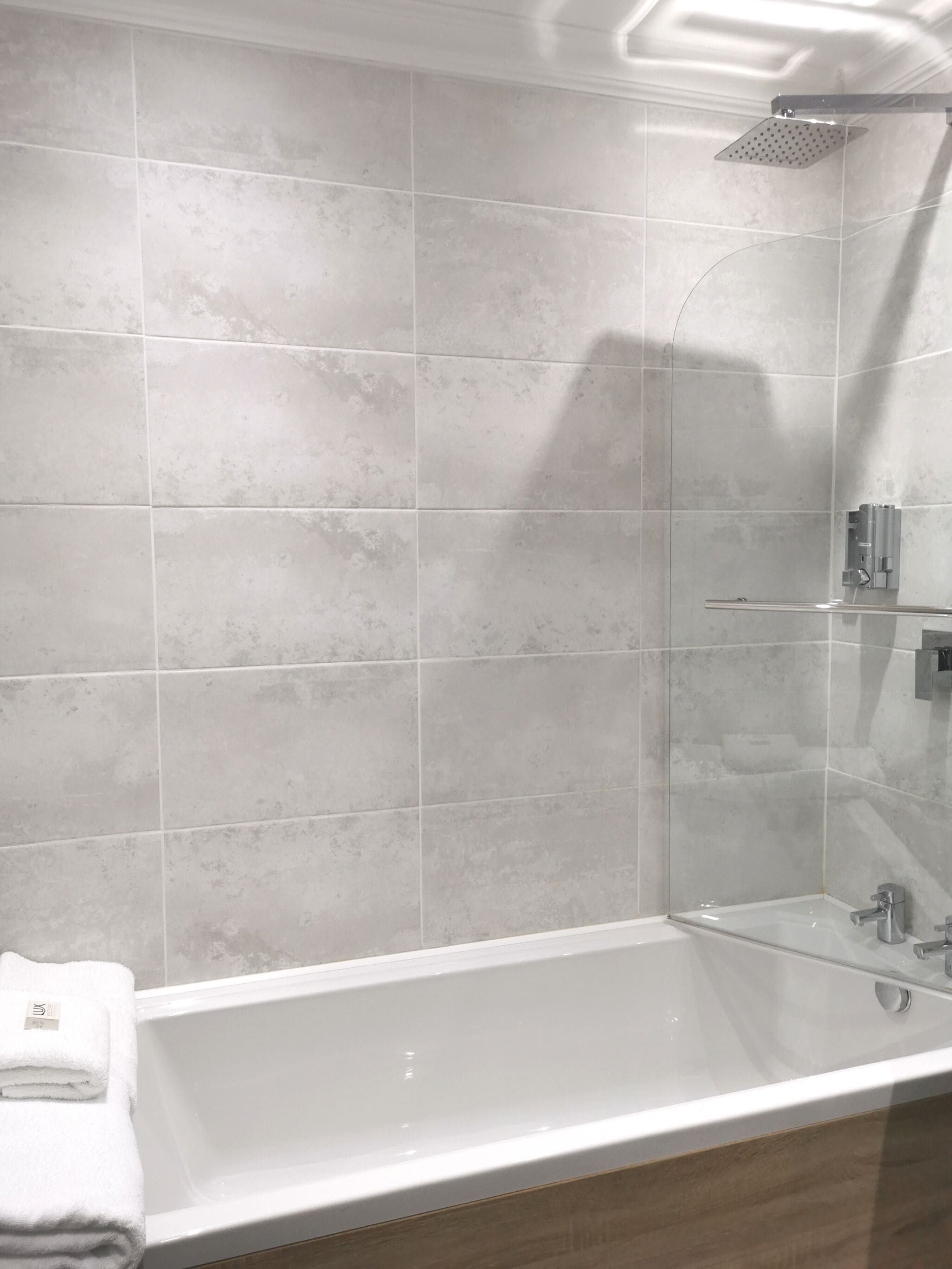 A modern bathroom with a glass-enclosed shower, a white bathtub, and a towel on the side.