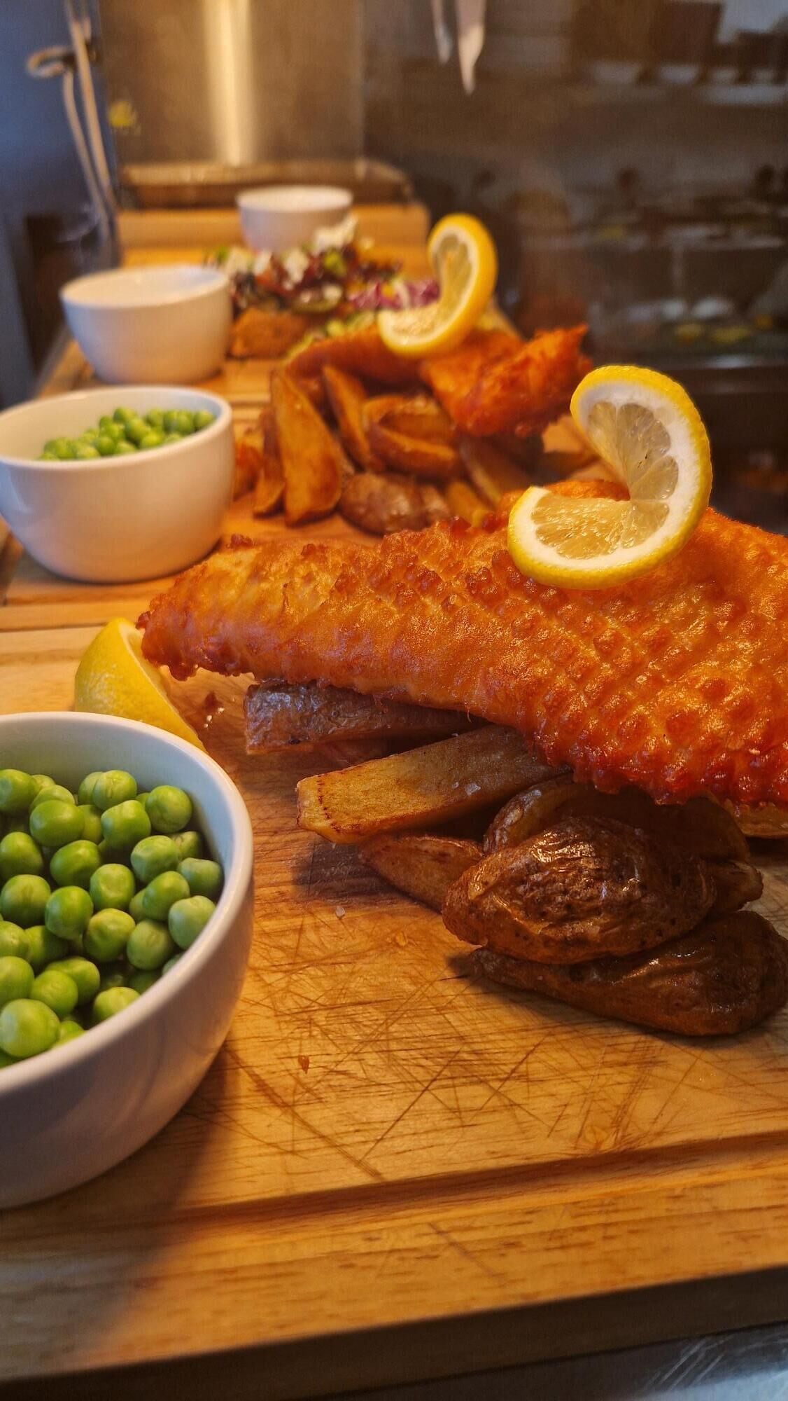 Een maaltijd met vis, friet en doperwten op een houten plank.
