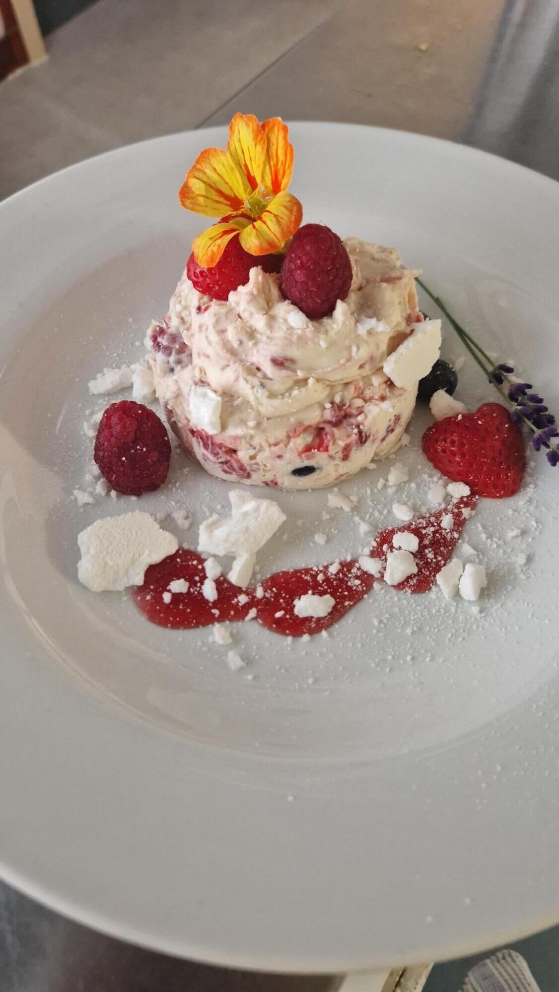A dessert on a white plate with raspberries, a flower, and powdered sugar.