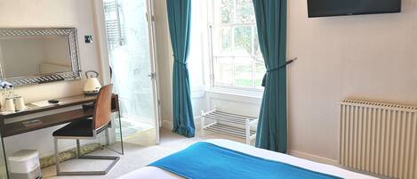 Una habitación de hotel con una cama, un escritorio con silla, un espejo, un televisor y una ventana con cortinas.