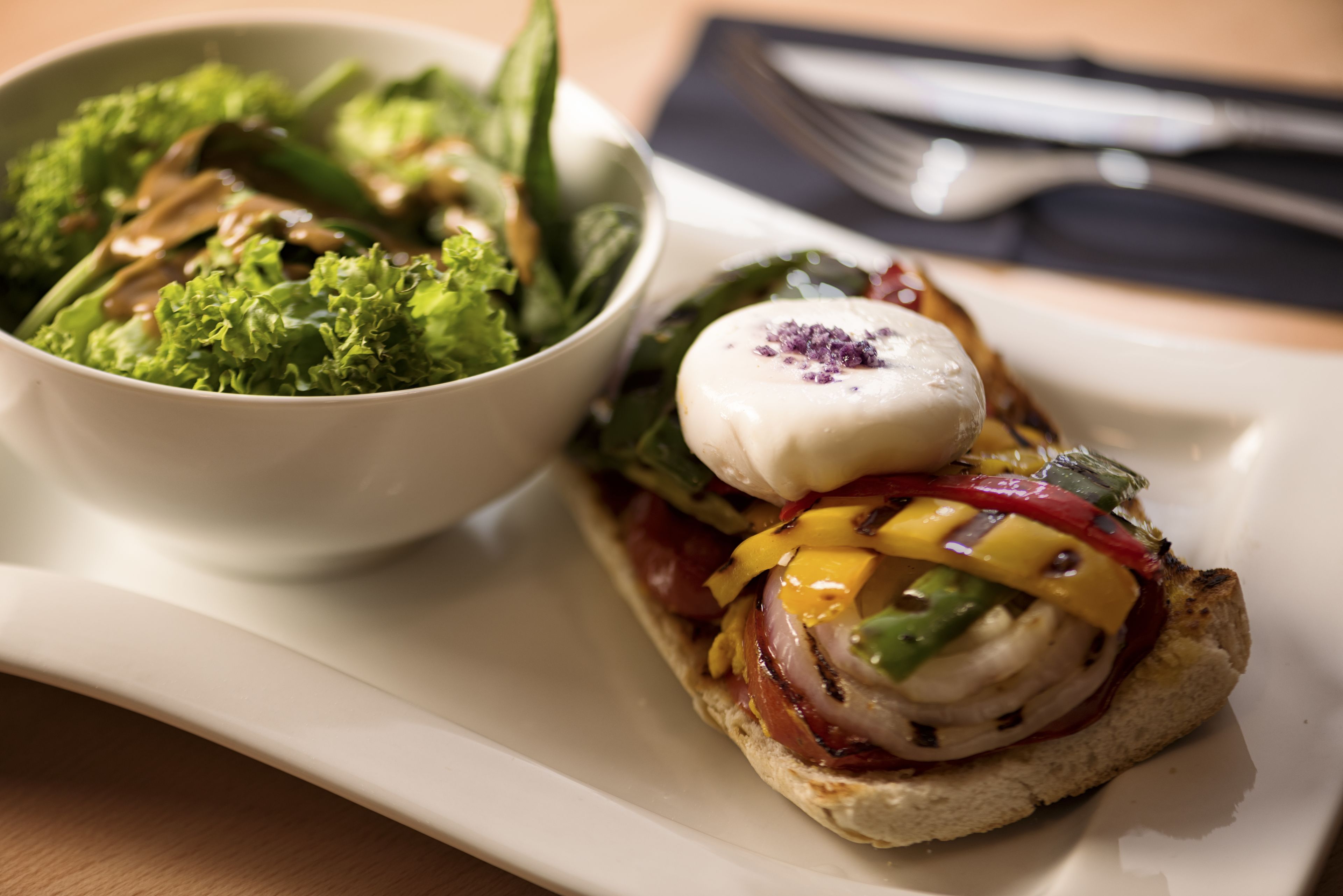 A sandwich with various toppings and a side salad on a white plate.