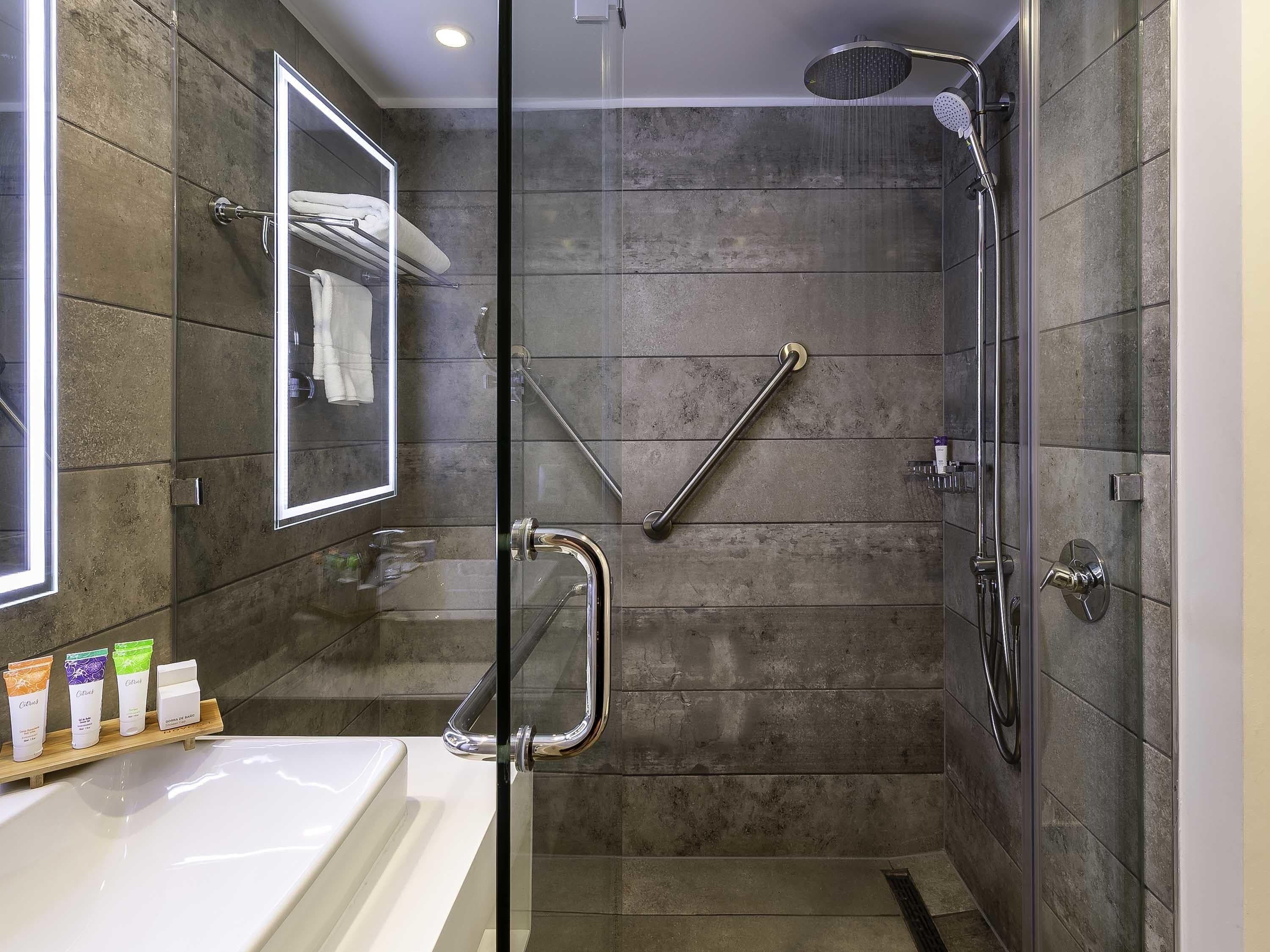 Een moderne badkamer met een douchecabine van glas, een glazen deur, een handgreep, een handdoekhouder en een plank met toiletartikelen.