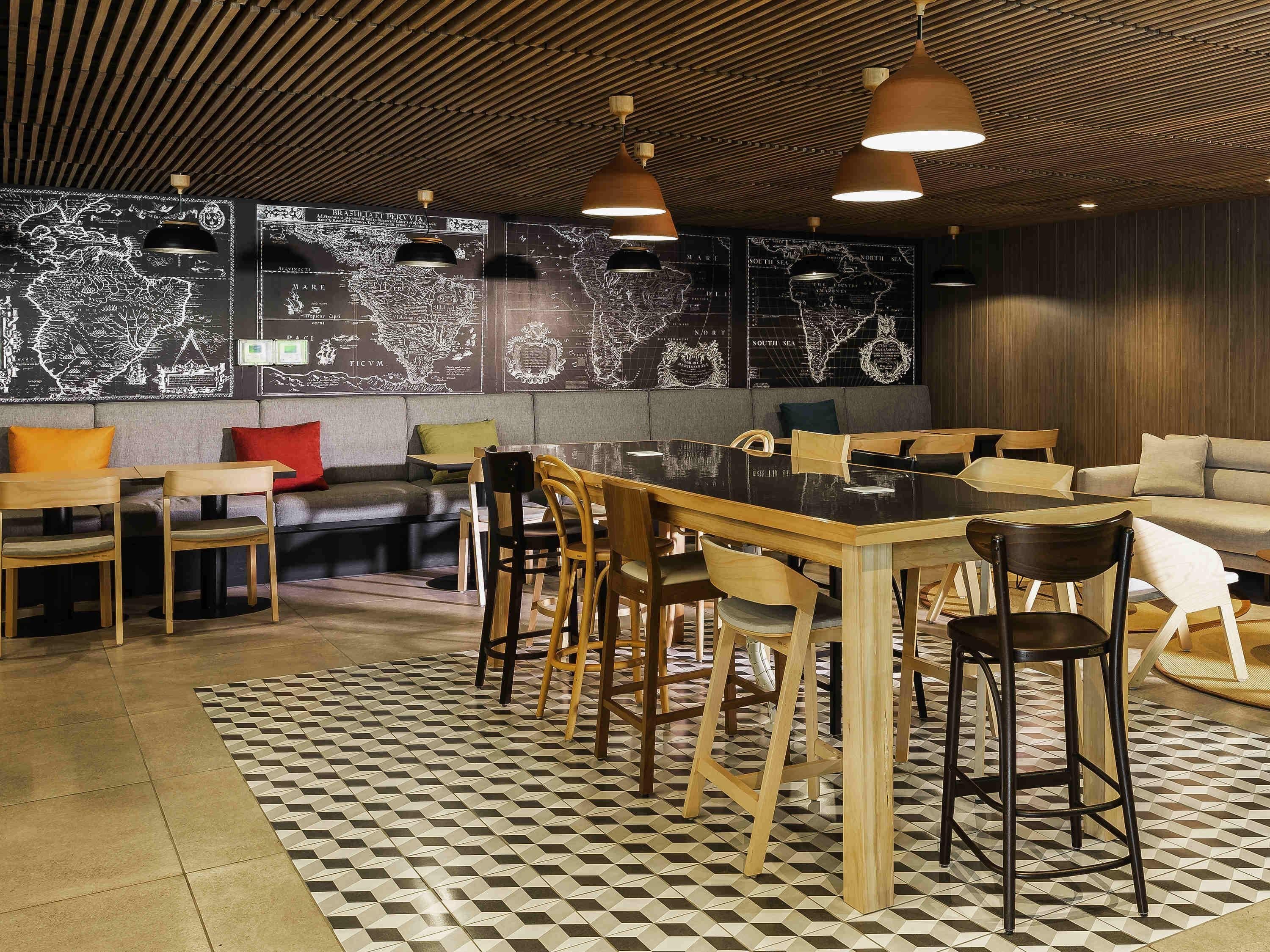 A modern dining area with a wooden table and chairs, a patterned floor, and a wall with maps.