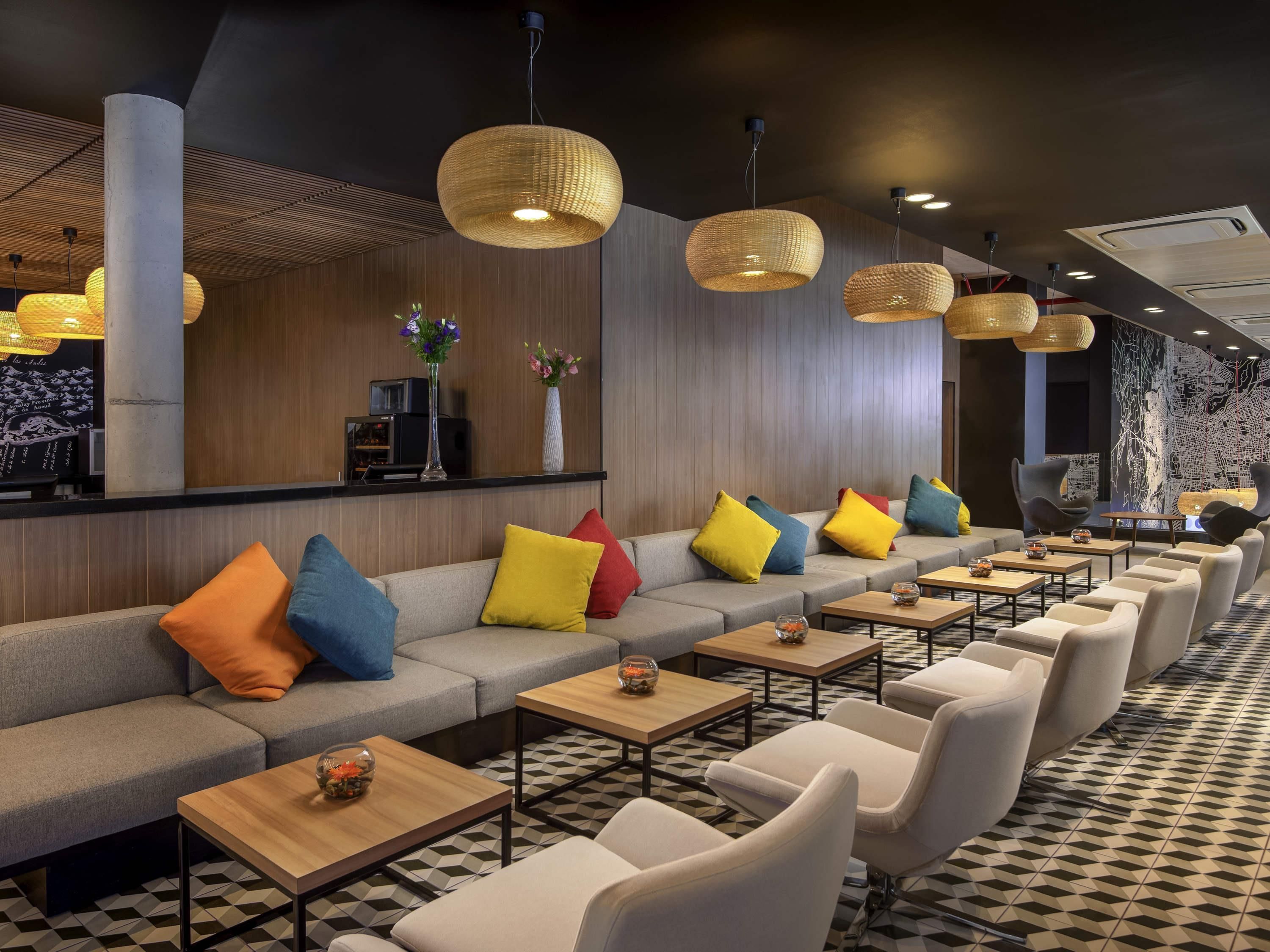 A modern lounge area with a sofa, chairs, tables, and hanging lights.